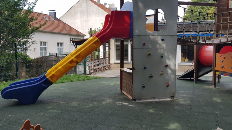 Auf einem öffentlichen Kinderspielplatz wurden unter dem Spielturm mit Rutsche, Kletterwand und Hängebrücke WARCO Fallschutz-Puzzlematten in der Farbe Grasgrün verlegt.