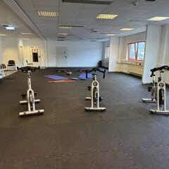 Gymnastikraum mit Crosstrainern auf braunen Warco-Platten. Turnverein hat  große Halle mit Fitnessmatten belegt.
