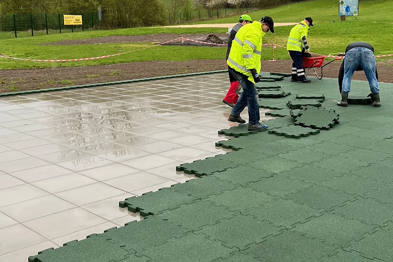 Un groupe d'ouvriers pose les dalles d’extérieur à clipser en couleur vert gazon de WARCO sous la pluie dans une zone carrelée.