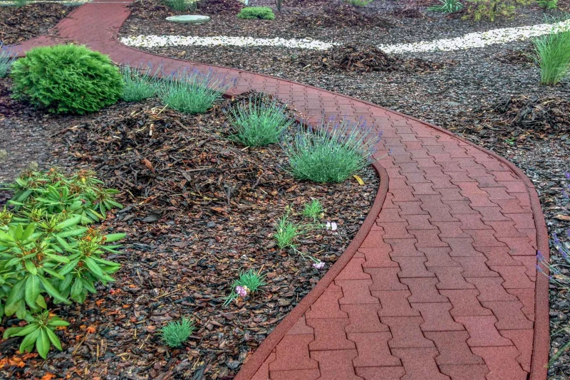 Un chemin de jardin courbé, de dalles en caoutchouc WARCO en couleur Café au lait, passe devant la maison en traversant le jardin.