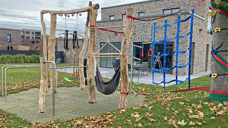 La structure d'escalade accrochée à un arbre avec des filets. A côté, quelques poteaux en bois avec un sac de frappe, une barre fixe et une balançoire.