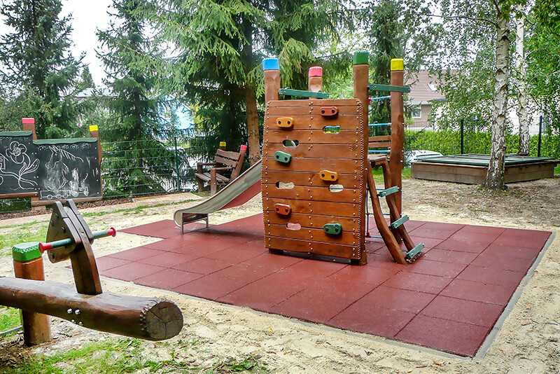 Sur une aire de jeux, il y a un sol antichoc WARCO avec des équipements de jeu en bois comme tour escalade avec toboggan.