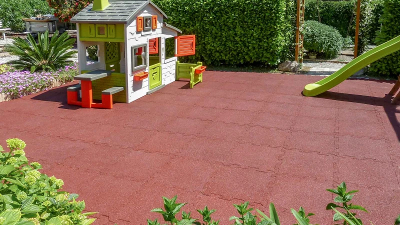 L'aire de jeux avec la maisonette dans le jardin privé. Une aire de jeux pour les enfants dans le jardin. Sur un vaste terrain en dalles amortissantes rouges de sécurité WARCO a été installée une maisonette en plastique.