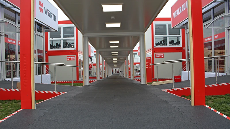Un parcours couvert mène aux différentes zones thématiques des journées d'information Würth 2019. Toutes les surfaces au sol sont recouvertes des dalles noires d'exposition WARCO.