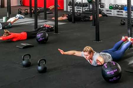 Des personnes allongées sur le sol élastique font de l'exercice dans un gymnase. Le sol est constitué de tapis sportifs de portection WARCO.