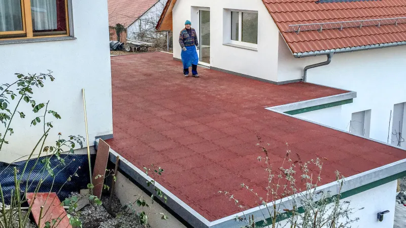 Entre deux maisons unifamiliales, il y a un garage avec un toit plat qui est conçu comme une terrasse constituée de dalles rouges de WARCO.