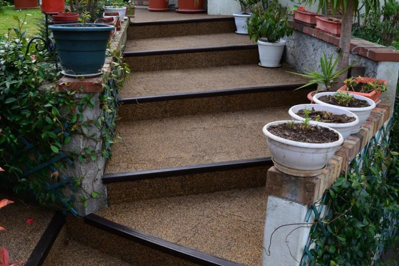 braune Treppe im Garten führt an Blumenkübeln vorbei Richtung Terrasse im Garten. Warco-Treppenbelag macht sie trittsicher.