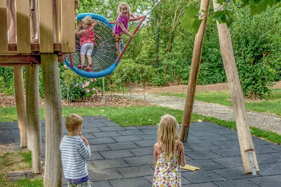 Fallschutzmatten unter einem Kletterhaus mit Rutsche und Nestschaukel auf dem Spielplatz.