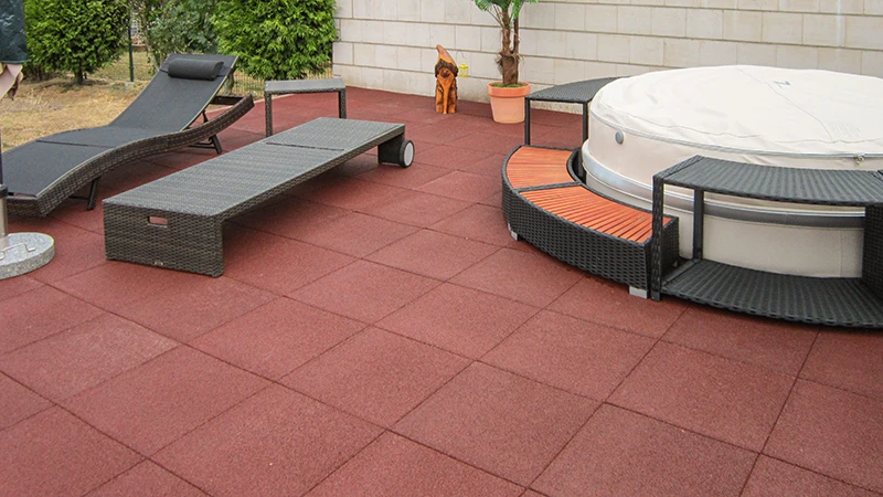 Eine großzügige Outdoor-Fläche mit roten WARCO-Terrassenplatten aus pu-gebundenem Gummigranulat, die für angenehme Trittsicherheit und strapazierfähigen Komfort sorgen. Darauf stehen bequeme Gartenmöbel und ein Whirlpool, der sich harmonisch ins Gesamtbild einfügt. Der elastische Bodenbelag dämpft Schritte, ist witterungsbeständig und pflegeleicht. Zudem überzeugt er durch seine rutschhemmende Oberfläche. Eine attraktive Lösung für stilvolles Entspannen im Freien.