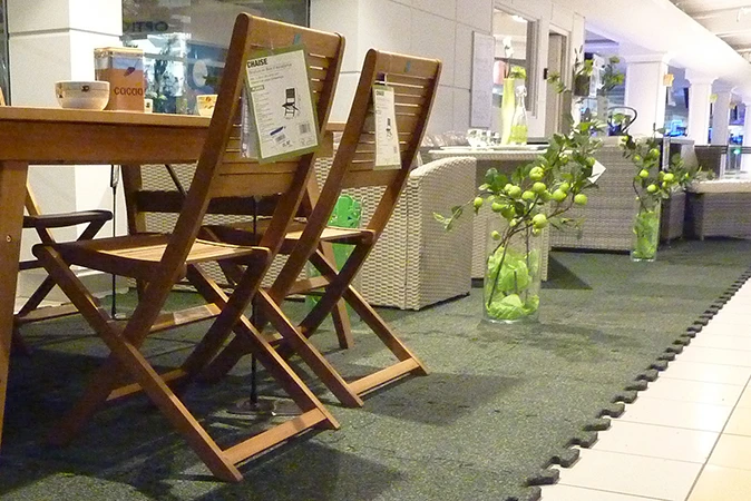 Im Einkaufszentrum wurde ein Teil der gekachelten Allee für den Sonderverkauf von Gartenmöbeln abgetrennt. Die Gartenmöbel stehen auf grünen Messeboden Klickfliesen.