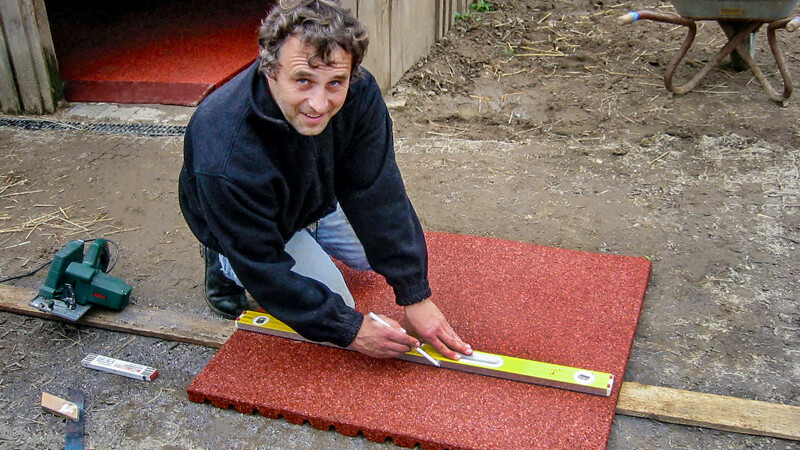 Un homme veut couper un tapis décurie rouge WARCO. Il trace la ligne de coupe avec un crayon, guidé par un niveau à bulle